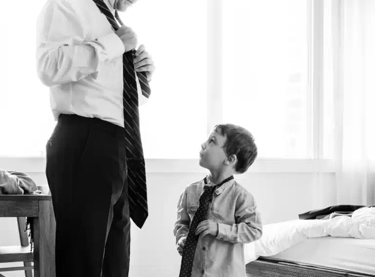 Petit garçon apprenant à nouer sa cravate avec l'aide de son père.Les grands chez les petits